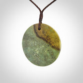This piece is a large sized, oval round, disc pendant. It is suspended on a chocolate brown coloured braided cord that is length adjustable.